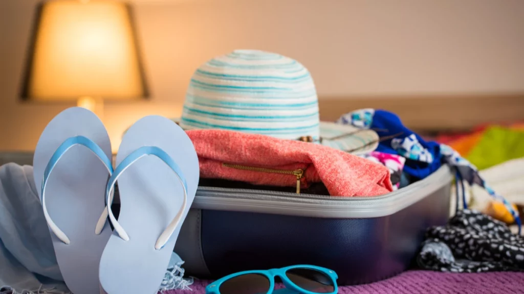 A suitcase with a hat, slides, dresses and sunglasses.