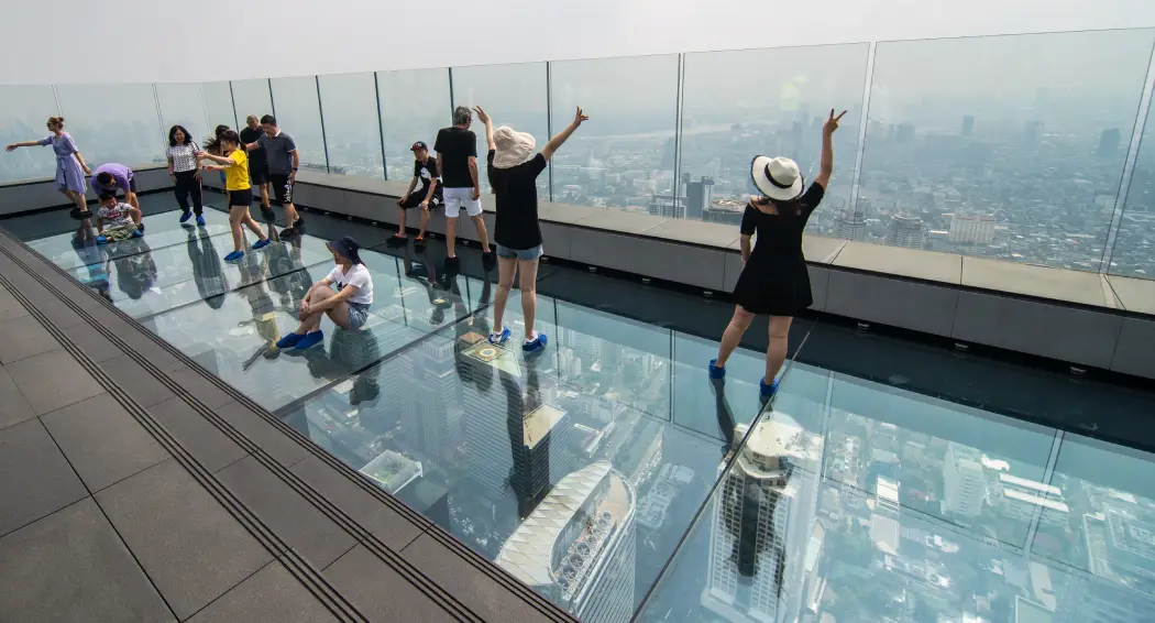 Tourists enjoying the stunning Bangkok skyline from the Mahanakhon Skywalk Glass Tray, dressed in comfortable clothing for an enjoyable experience