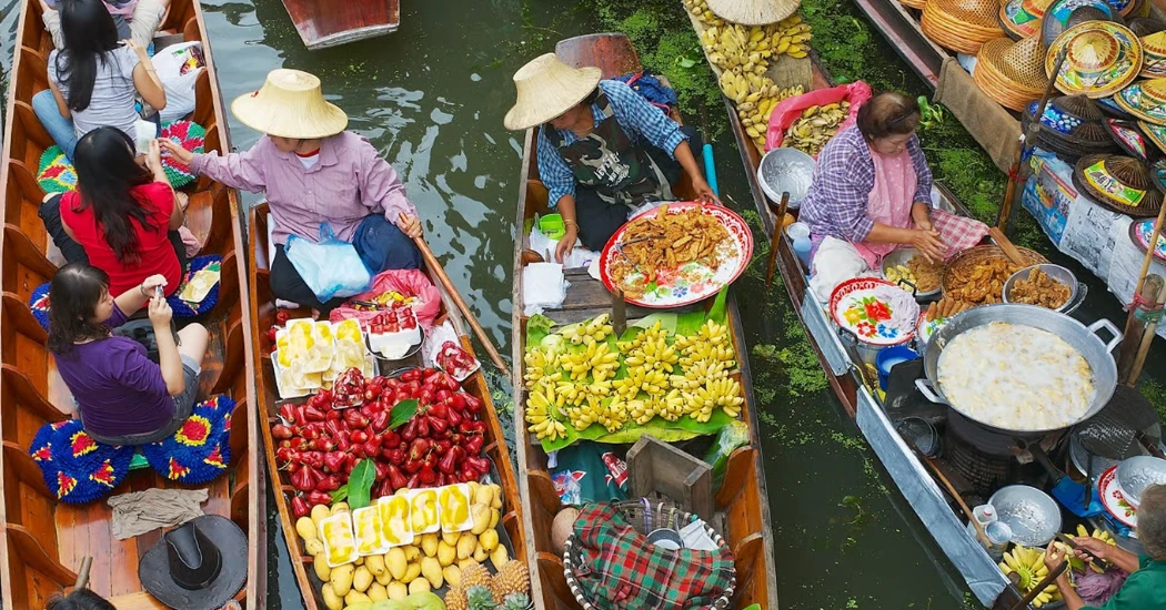 Vendors selling fruits and snacks from boats at Damnoen Saduak Floating Market.