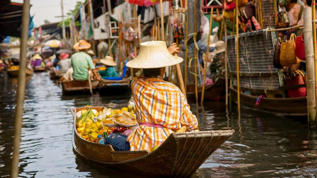 Ein Händler rudert in einem kleinen Holzboot voller Früchte durch einen geschäftigen schwimmenden Markt in Thailand. Ein Händler rudert in einem kleinen Holzboot voller Früchte durch einen geschäftigen schwimmenden Markt in Thailand.