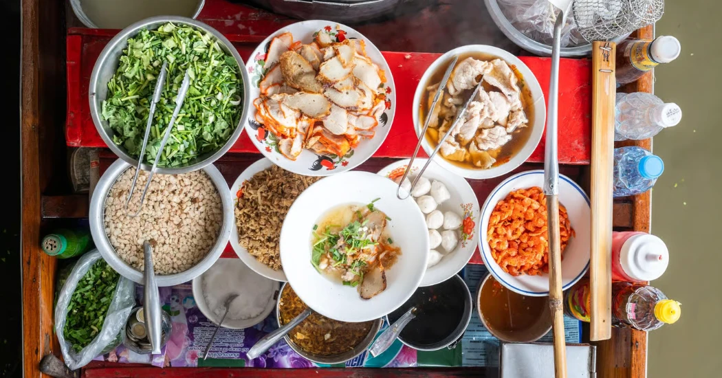 A bowl of Thai noodles with toppings being served from a boat at the floating market.