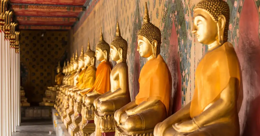 Row of golden Buddha statues along a decorated wall inside Wat Pho
