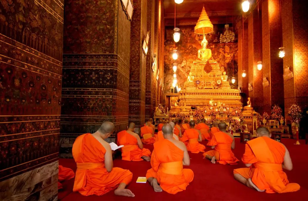 A group of monks in bright orange robes performing a prayer session at Wat Arun